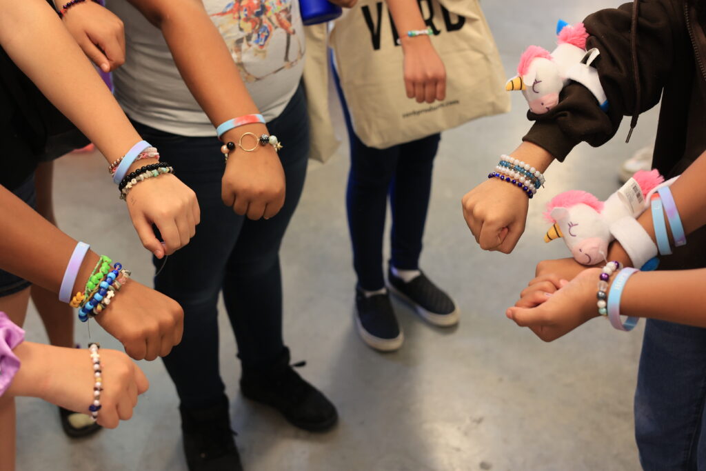 7 members of the SMART girls program extend their wrists to the camera showing off friendship bracelets they've made