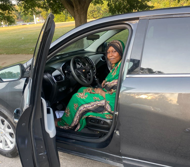 A woman in African clothing sits in the front-seat of car supplied by Wheels of Hope with the door open